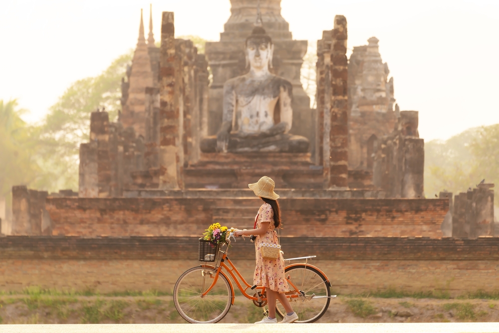 Woman with bike in front of ancient temple and Buddha statue