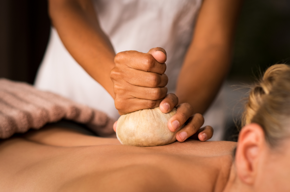 A close-up of a masseuse’s hand pressing pinda massage on a woman’s back