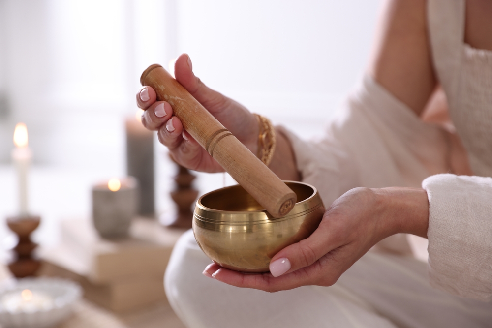 A woman with a gold bowl and a wooden stick for sound healing