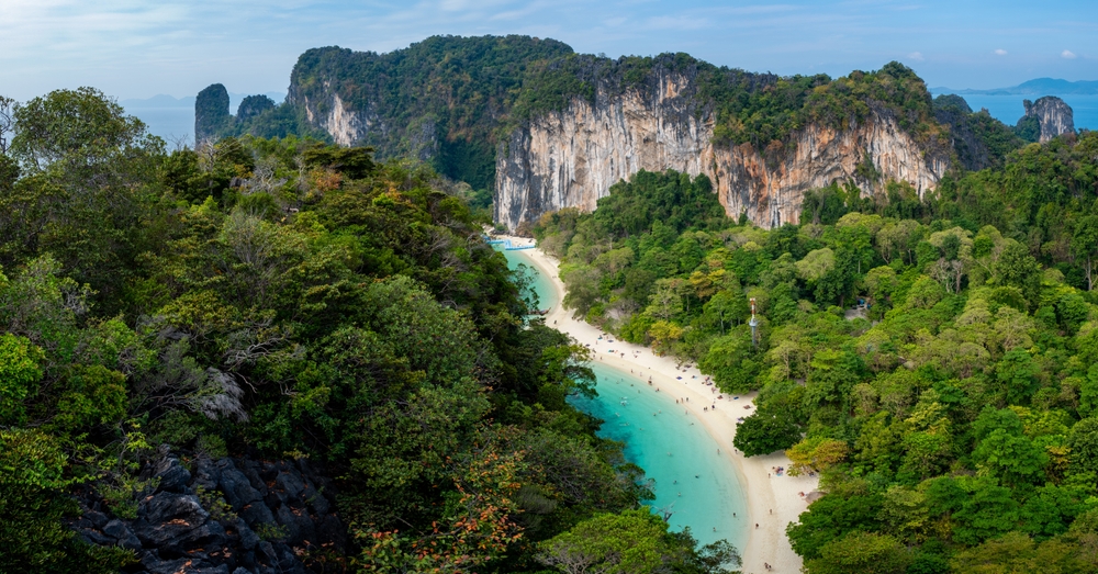 Towering cliff and lush greenery surround a white sand beach and crystal-clear water in Koh Hong, Krabi, Thailand
