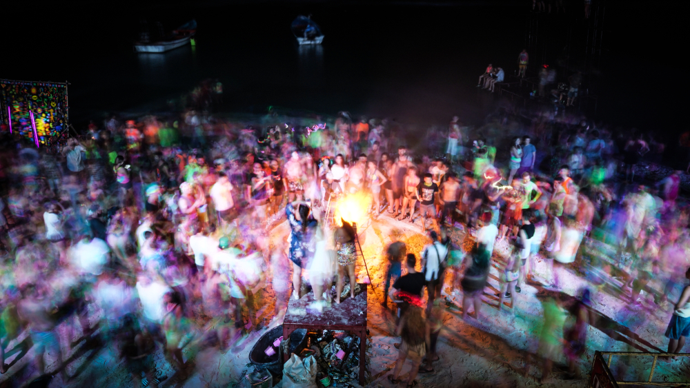 A crowd of people watching a fire show on the beach at full moon party night