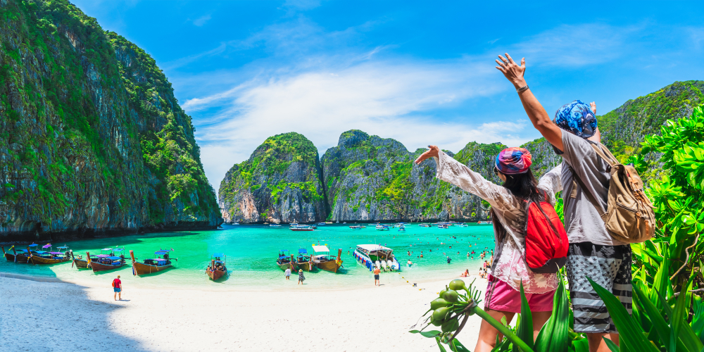 Two happy travelers looking at the white sand beach at Maya Bay and the surrounding limestone cliffs in Koh Phi Phi