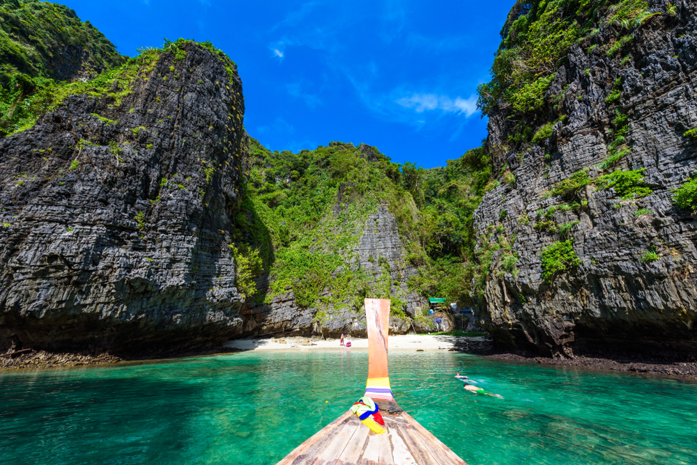A part of a longtail boat on turquoise water with towering cliffs going into Wang Long Bay in Koh Phi Phi