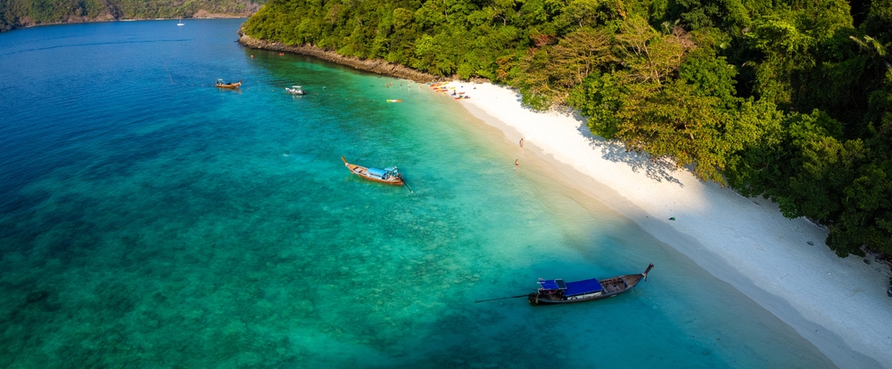 aerial view of Monkey Beach with white sand beach and long tail boats on turquoise sea waters