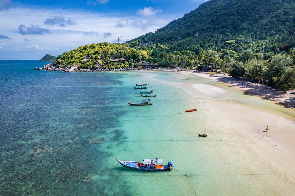 Aerial view of Sairee Beach on Koh Tao, with longtail boats anchored near the white-sand beach and crystal-clear waters