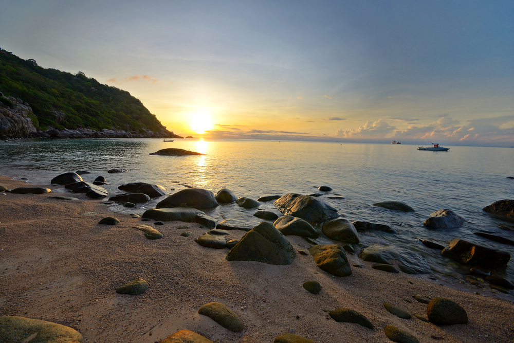 Many rocks on a sandy beach next to sea during sunset at Aow Luek on Koh Tao