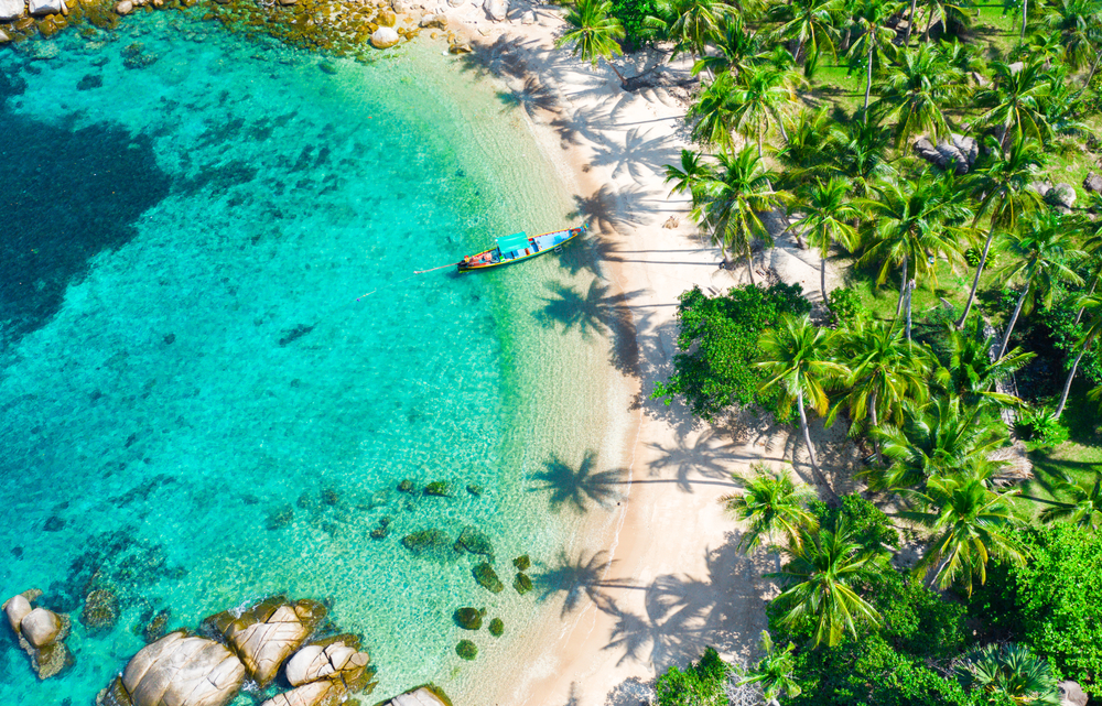 Top view of Sia Nuan Beach on Koh Tao, where a longtail boat is floating on clear waters and lush vegetation covers the land