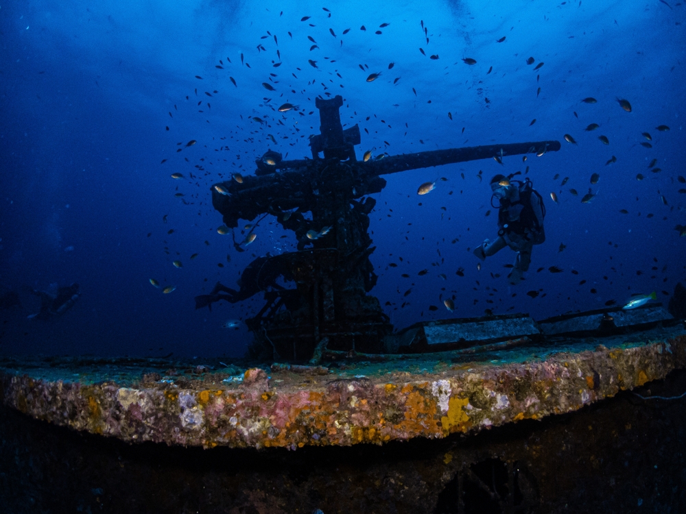 Part of the HTMS Sattakut wreck with schools of fish and a diver in the back in Koh Tao