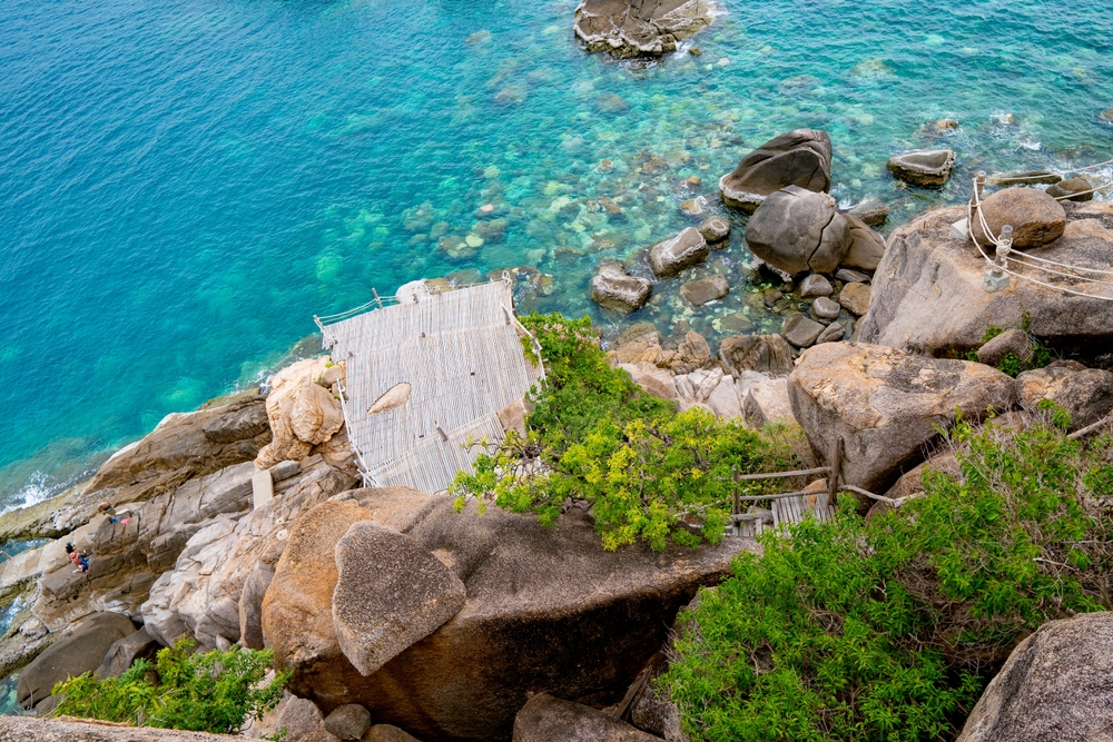 Aerial view overlooking the wooden deck coming out of rocky boulders above the sea at Moondance Magic View in Koh Tao