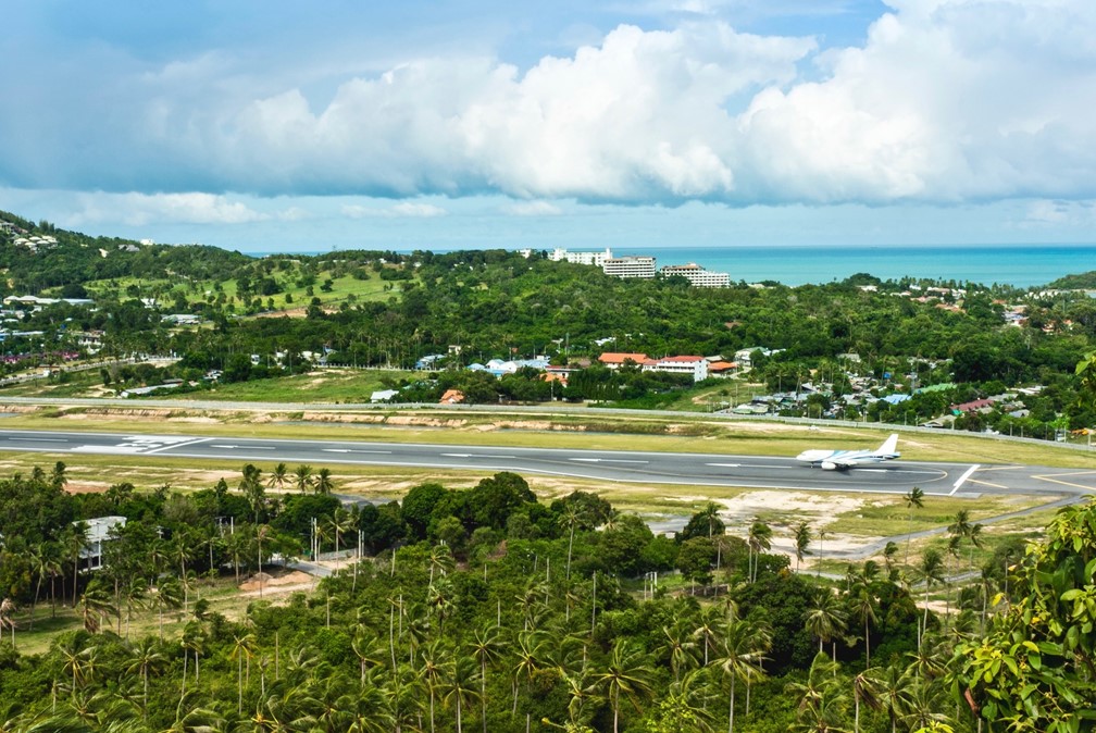 Aerial view of an airplane on the Samui International Airport runway surrounded by tropical forests.