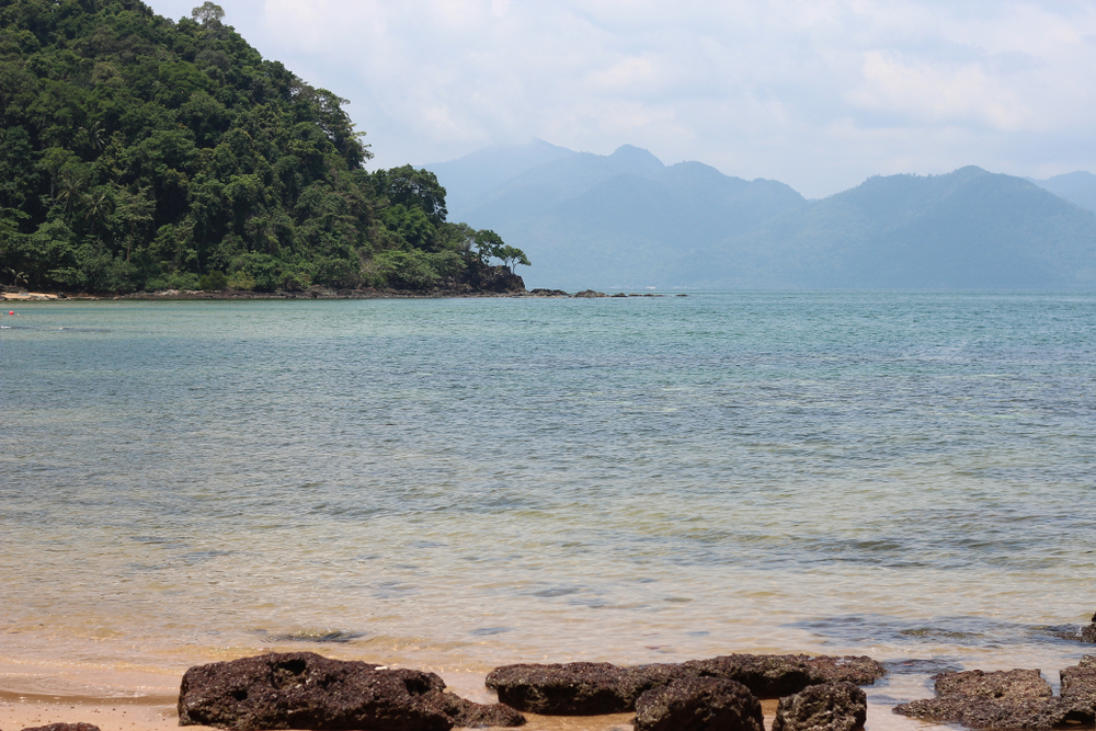 วิวริมชายหาดอ่าวตาลคู่ มีโขดหินสีเข้มอยู่ด้านหน้า ถัดไปเป็นน้ำทะเลใสและแนวเทือกเขา