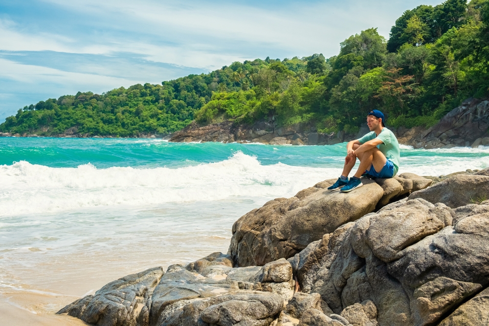 นักท่องเที่ยวนั่งพักผ่อนบนโขดหินริมหาดฟรีดอม ภูเก็ต ท่ามกลางเกลียวคลื่นและธรรมชาติที่สวยงาม ในช่วงเวลาที่เหมาะกับการเที่ยวที่สุด