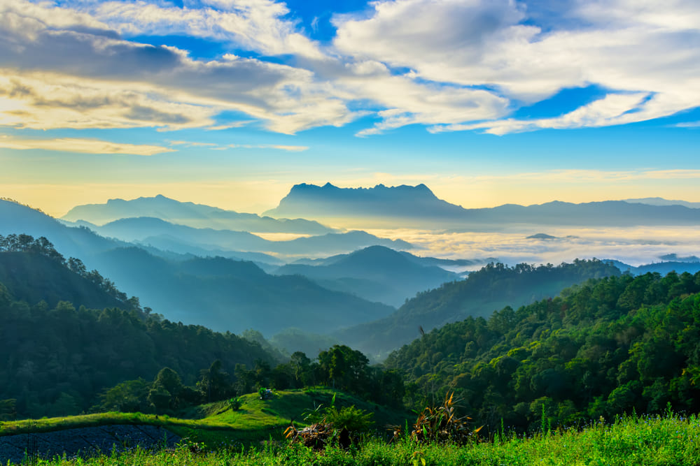 A panoramic view of the mist-covered Doi Luang Chiang Dao mountain and lush valleys in northern Thailand during the rainy season in Southeast Asia.