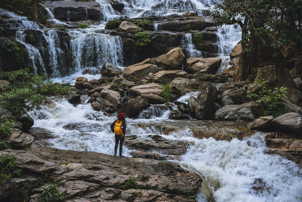 A traveler admiring the powerful Mae Ya Waterfall in Chiang Mai during the rainy season in Southeast Asia.