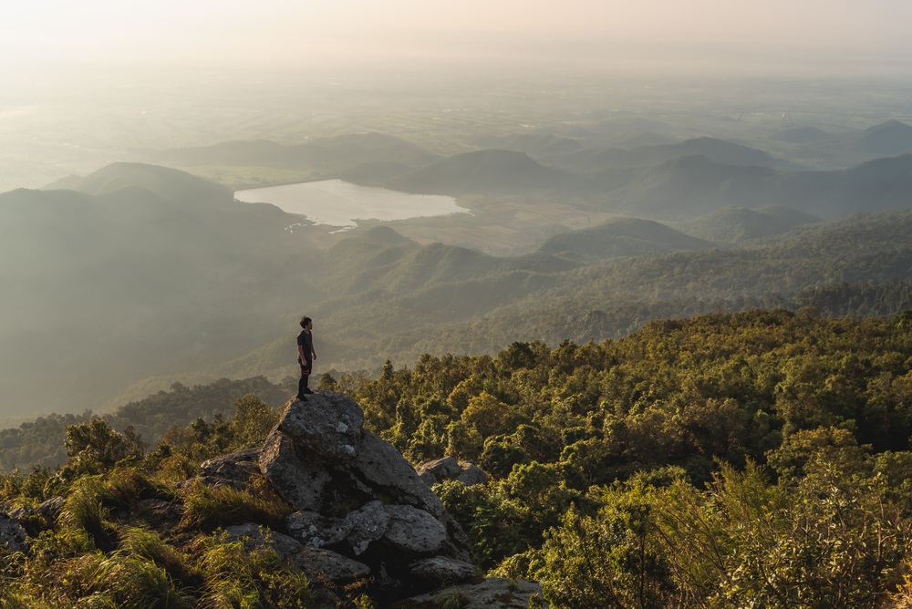 A hiker watching the mist over lush mountains at Khao Luang in Sukhothai during the rainy season in Southeast Asia.