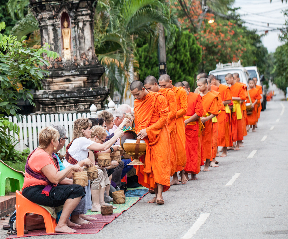 ขบวนพระสงฆ์เดินรับบาตรข้าวเหนียวจากกลุ่มนักท่องเที่ยวต่างชาติริมถนน หลวงพระบาง ประเทศลาว