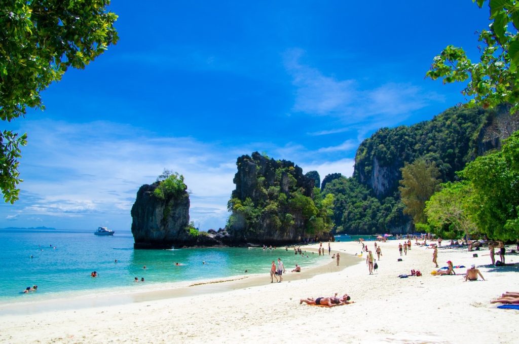 นักท่องเที่ยวพักผ่อนริมชายหาดโค้งสวยและน้ำทะเลสีมรกตที่เกาะห้อง มรกตแห่งอันดามัน จุดท่องเที่ยวแนะนำเมื่อมาทริปเกาะปอดะ กระบี่