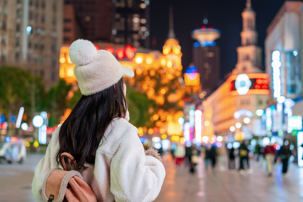 A tourist exploring the vibrant and illuminated Nanjing Road shopping street in Shanghai at night.