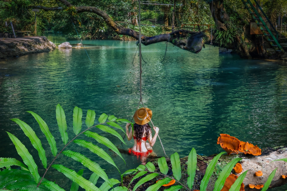 A tourist relaxing on a swing over the crystal-clear turquoise water at a Blue Lagoon in Vang Vieng.