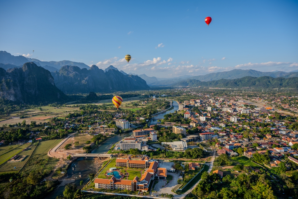 Hot air balloons flying over Vang Vieng town and the Nam Song River during a beautiful sunset.