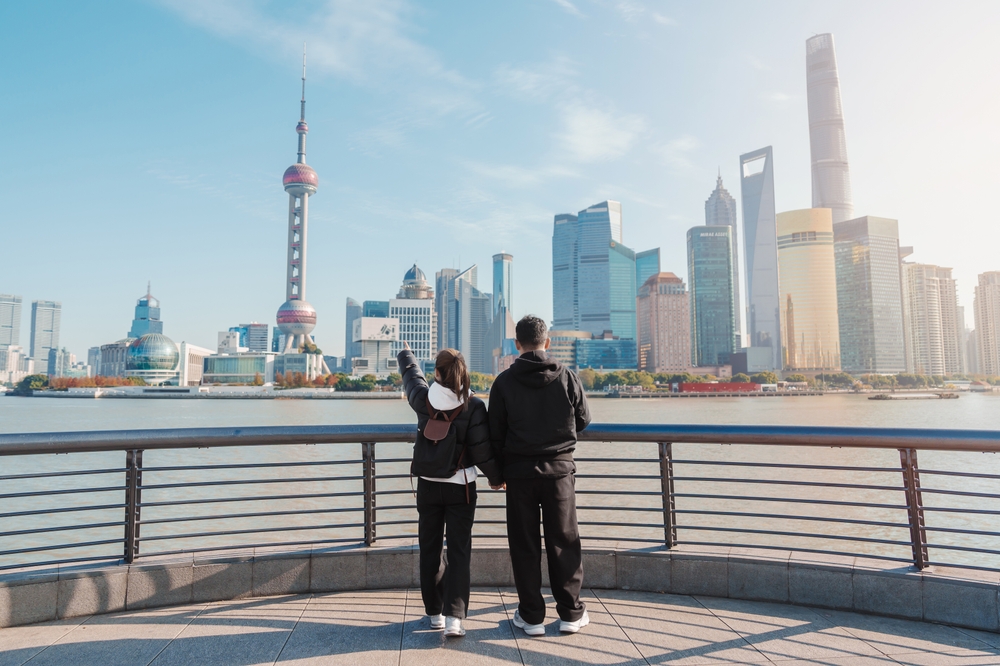 A couple admiring the Oriental Pearl Tower and Pudong skyline along the Huangpu River waterfront in Shanghai.