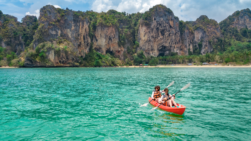 Tourists kayaking in the emerald sea surrounded by limestone cliffs near Ao Nang Beach in Krabi, Thailand.