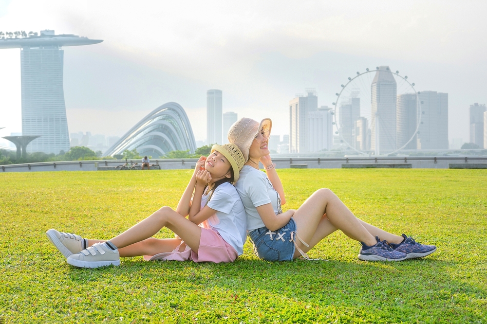 แม่และลูกนั่งพักผ่อนบนลานหญ้าของสิงคโปร์ในช่วงเวลาที่น่าเที่ยวและเหมาะกับการพักผ่อนแบบครอบครัว